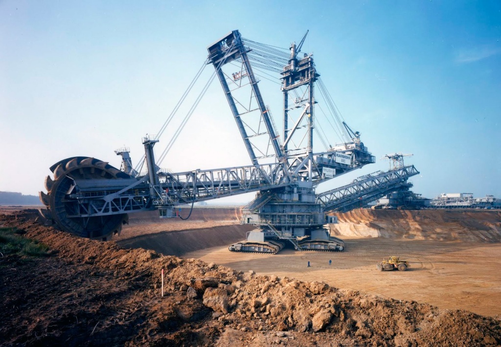 A colossal bucket-wheel excavator device. It looks kind of like a big shipping crane with a circular sawblade made of excavator buckets all frankensteined together. Some tiny people indicate the scale.